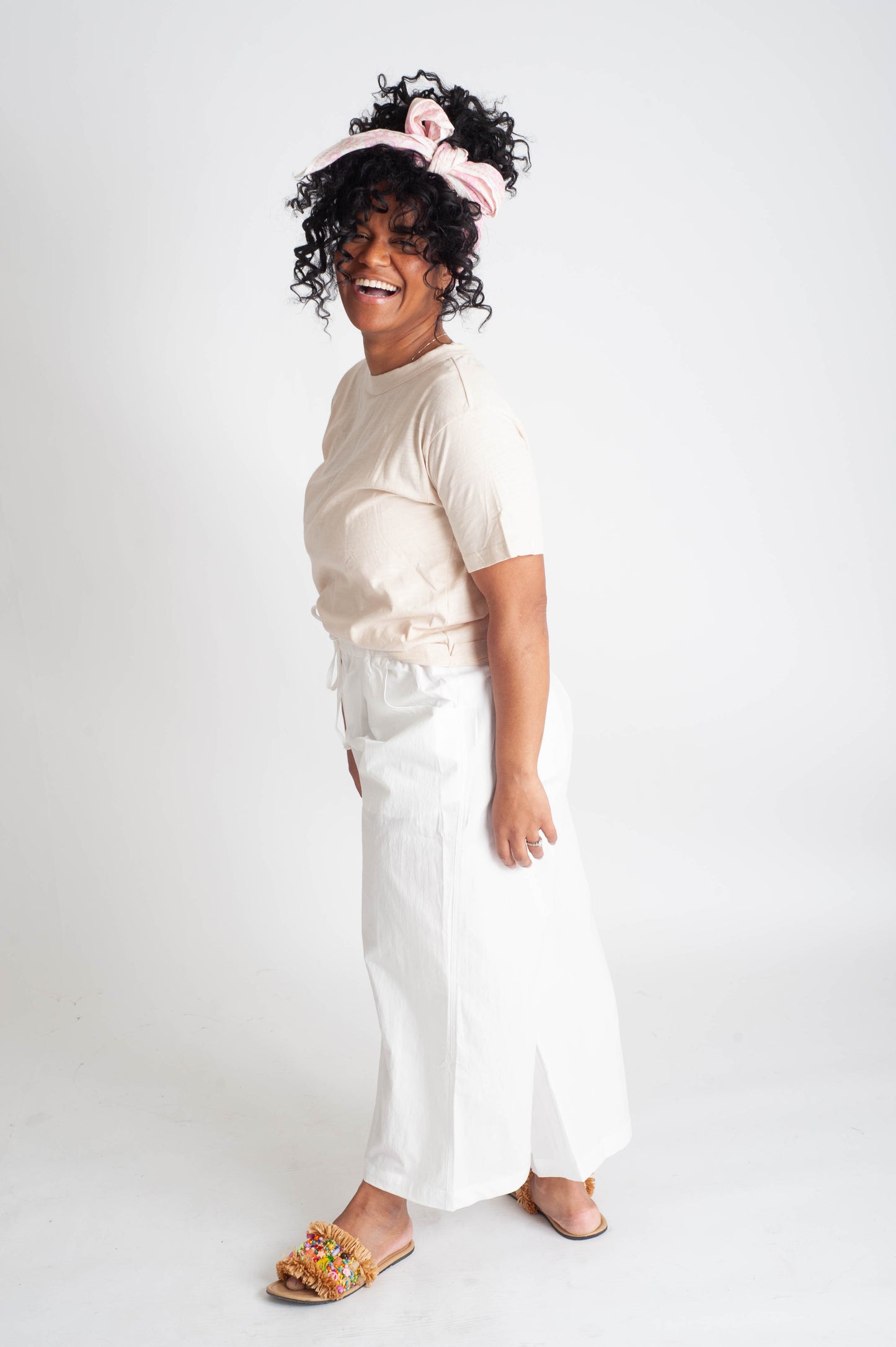 Woman wearing a beige top and white pants with a pink headband on a white background