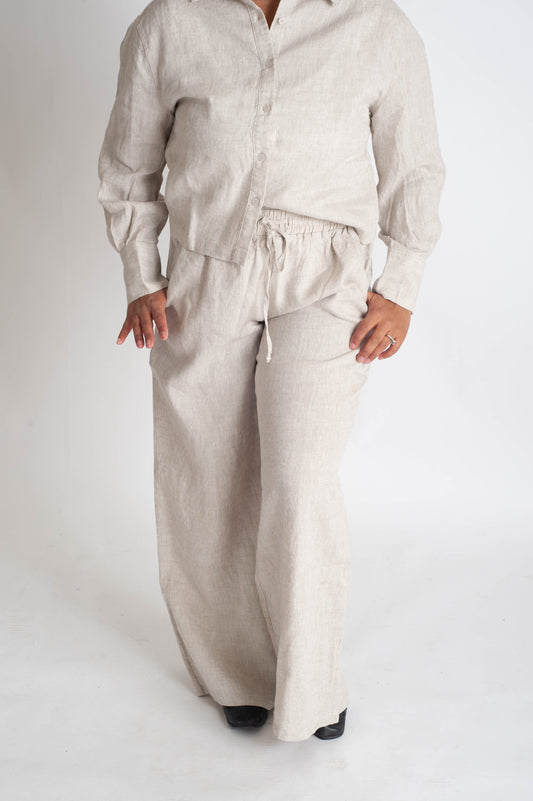 Person wearing a beige linen shirt and pants on a white background