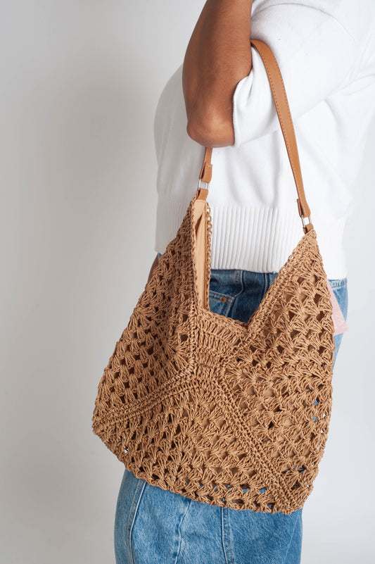 Brown crochet bag held by a person against a plain background