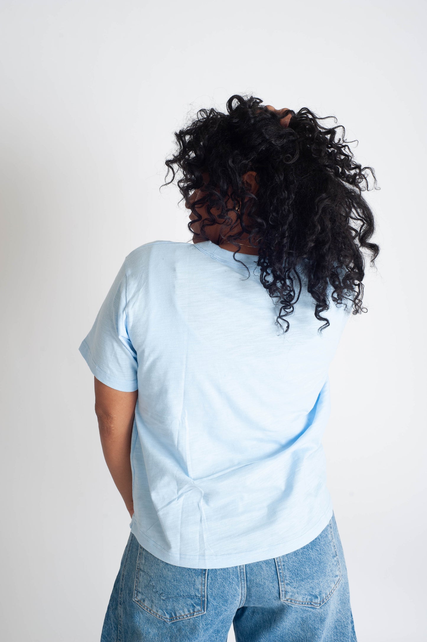 Person wearing a light blue shirt and jeans from behind on a white background