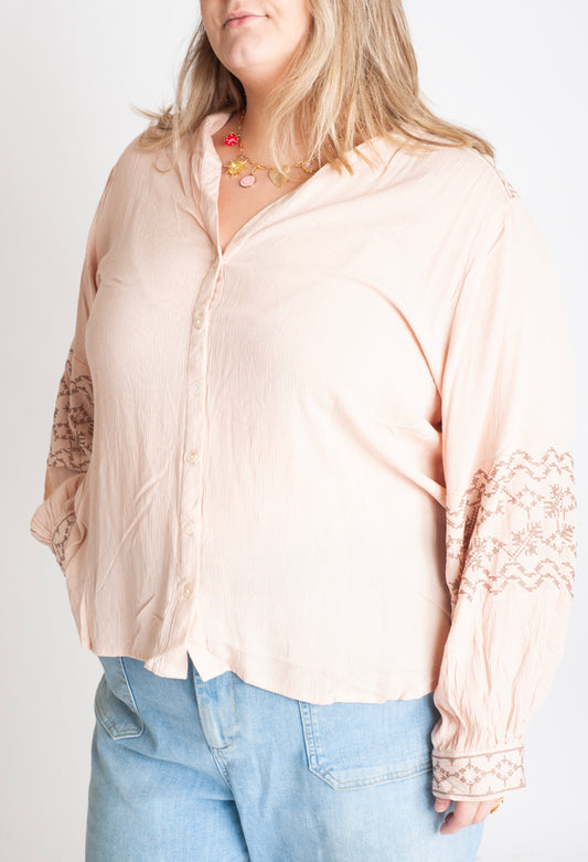 Woman wearing a beige blouse with lace sleeves and light blue jeans on a white background