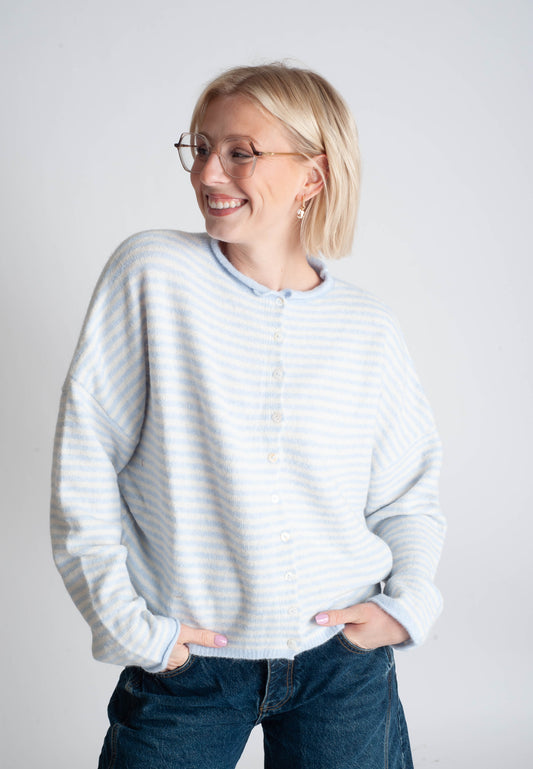 Woman wearing a light gray striped sweater and blue jeans against a white background