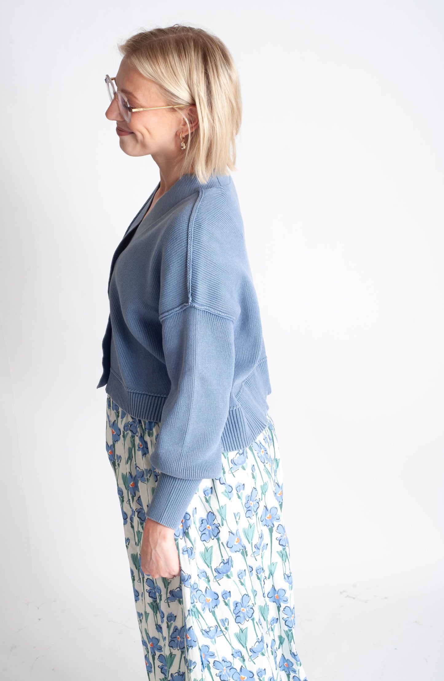 Woman wearing a blue cardigan and floral dress on a white background