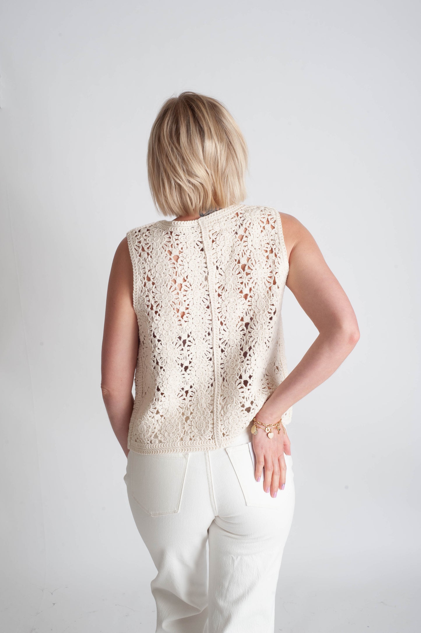 Woman wearing a beige crochet top and white pants on a plain background