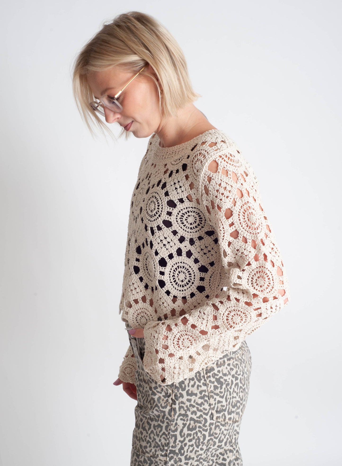 Woman wearing a beige crochet sweater with black patterns on a white background