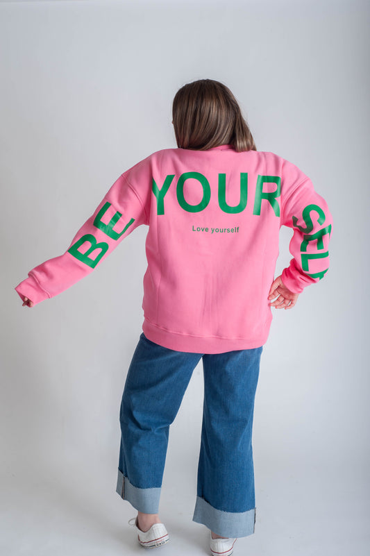 Person wearing a pink sweatshirt with 'BE YOURSELF' text on a white background