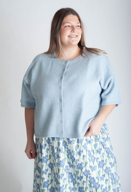 Women wearing a blue button up cardigan and blue floral skirt on a white background.