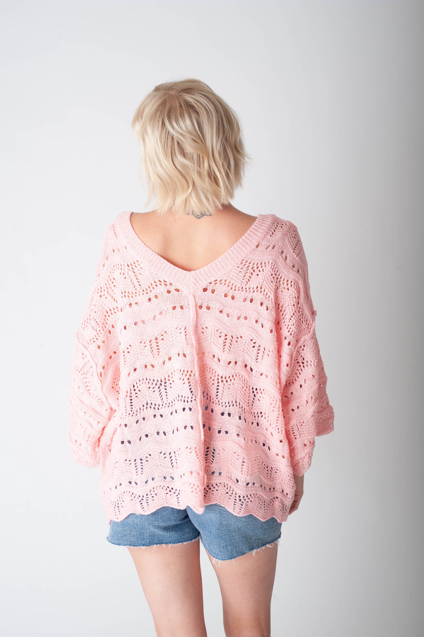 Women wearing a pink crochet sweater and denim shorts on a neutral background.