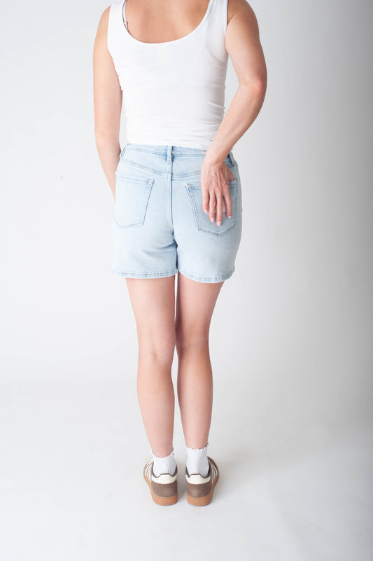 Women wearing long denim shorts and a white tank top.