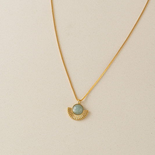Gold necklace with a green pendant on a beige background