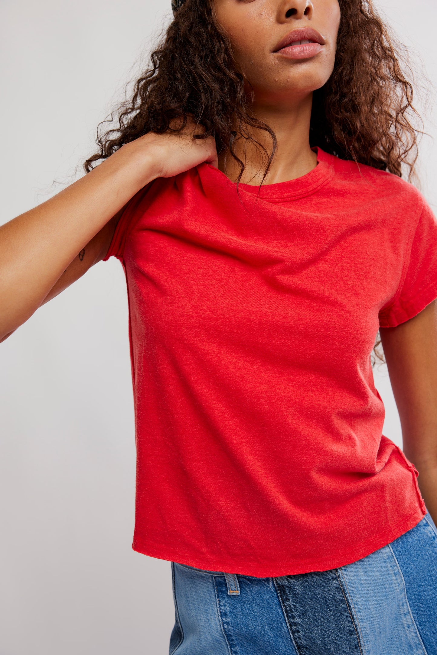 Person wearing a red t-shirt and blue jeans against a plain background