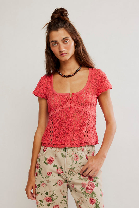 Woman wearing a red lace top and floral pants against a plain background