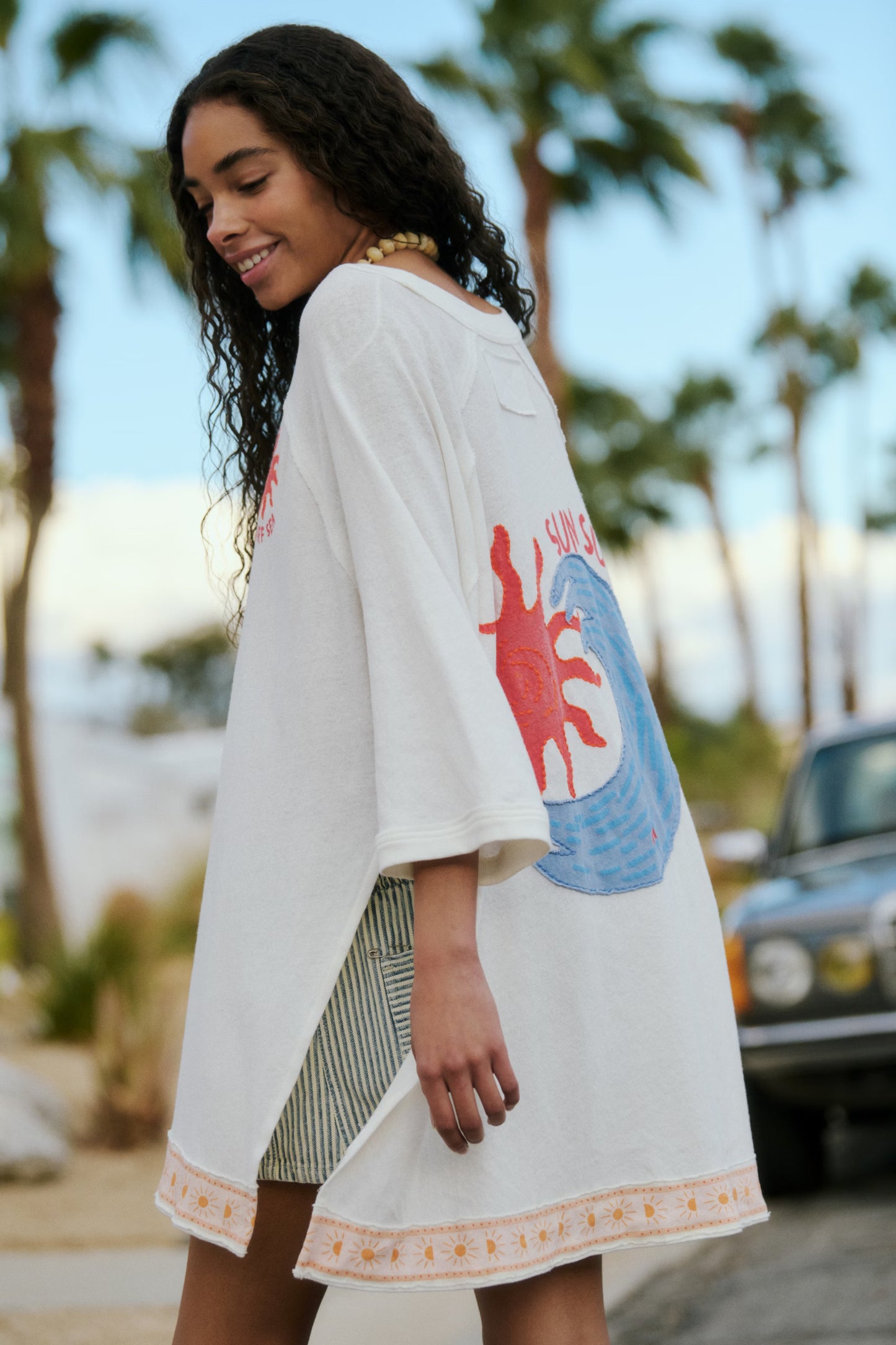 Woman wearing a white kimono-style garment with colorful designs in a tropical setting
