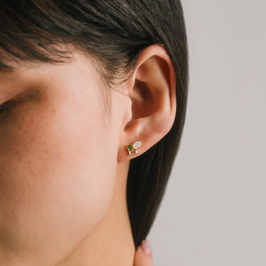 Close-up of a person wearing a gold earring with a green gemstone on a neutral background