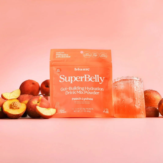 SuperBelly drink mix powder package with peaches and a glass of juice on a pink background