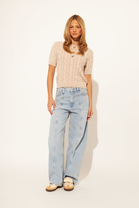 Woman wearing a beige cable knit sweater and light blue jeans on a white background
