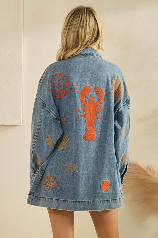 Denim jacket with lobster and shell designs on a neutral background
