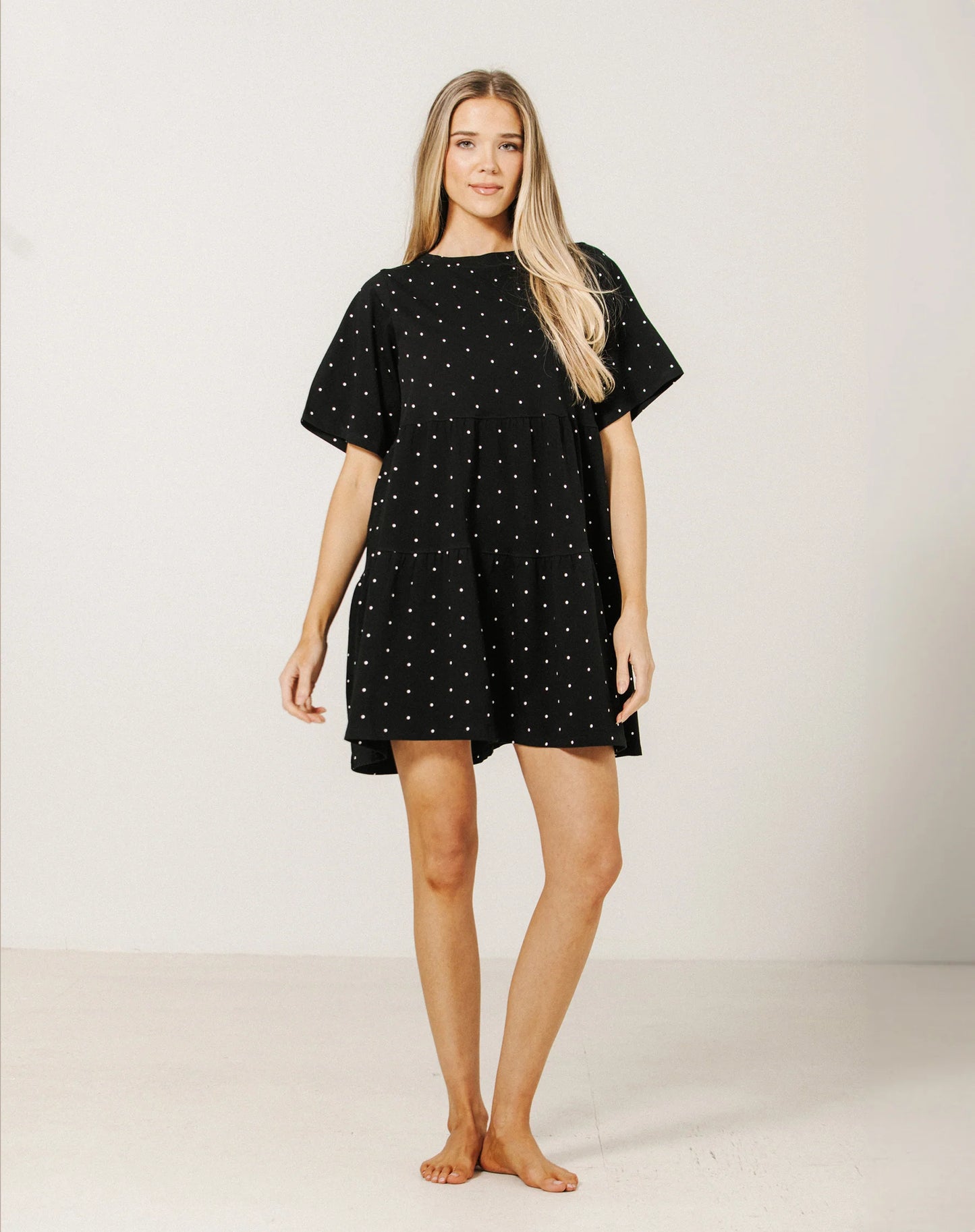 Woman wearing a black dress with white polka dots on a plain background