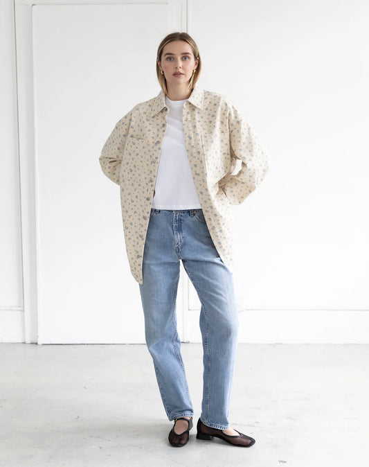 women wearing a blue floral denim jacket with blue jeans and white top on a plain background.
