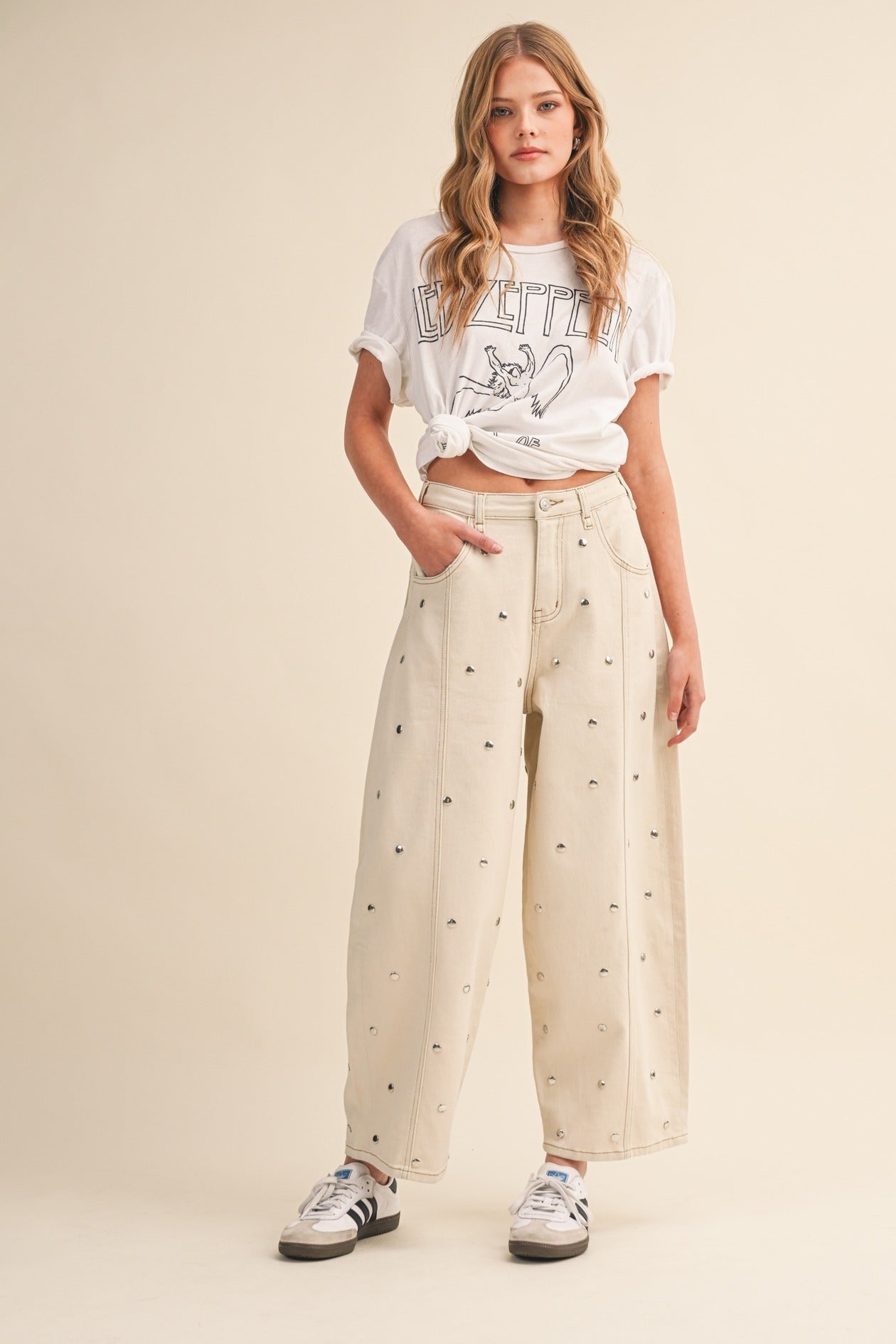 Woman wearing a white graphic t-shirt and beige pants with black patterns on a beige background