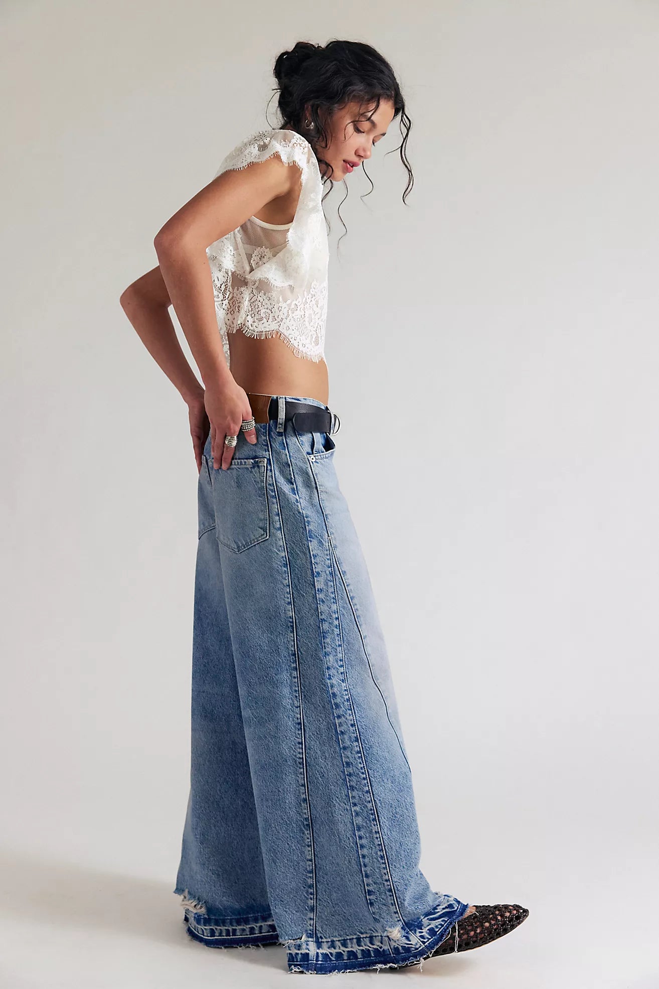 Woman wearing a white lace top and long blue jeans on a plain background