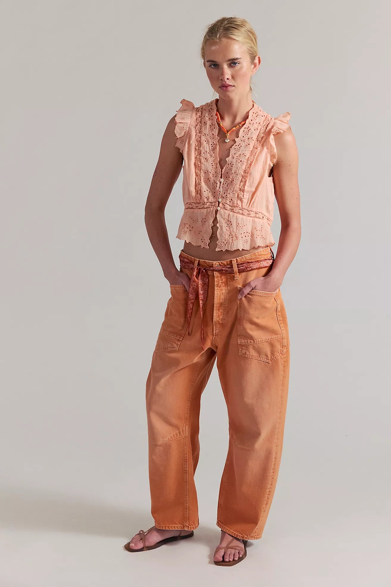 Woman wearing a peach-colored sleeveless top and pants on a plain background