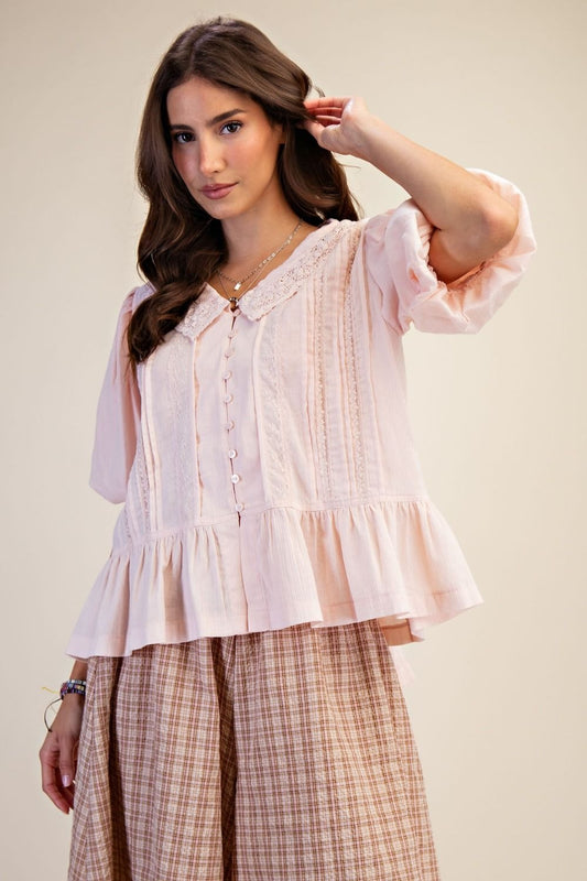 Woman wearing a light pink blouse with ruffled sleeves and plaid skirt against a plain background