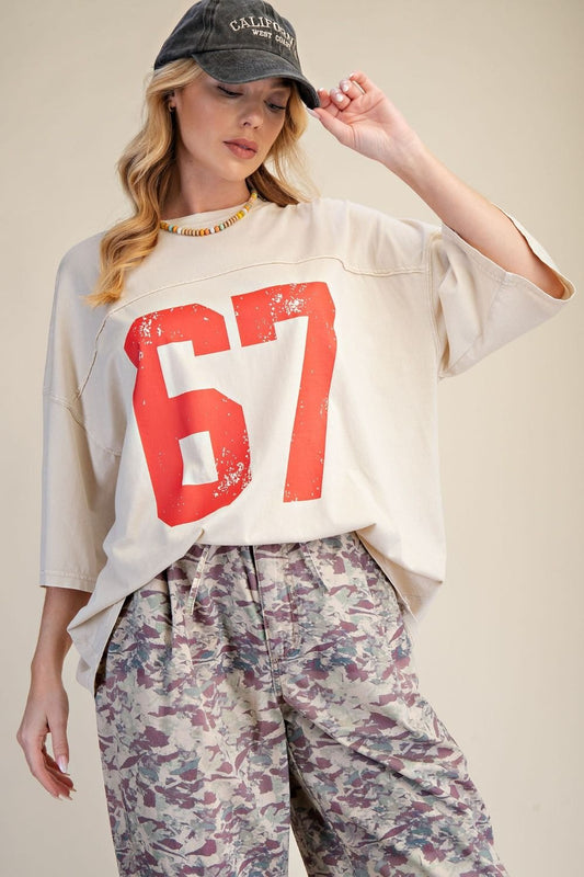 Woman wearing a white oversized shirt with red number 67, floral pants, and a cap on a beige background