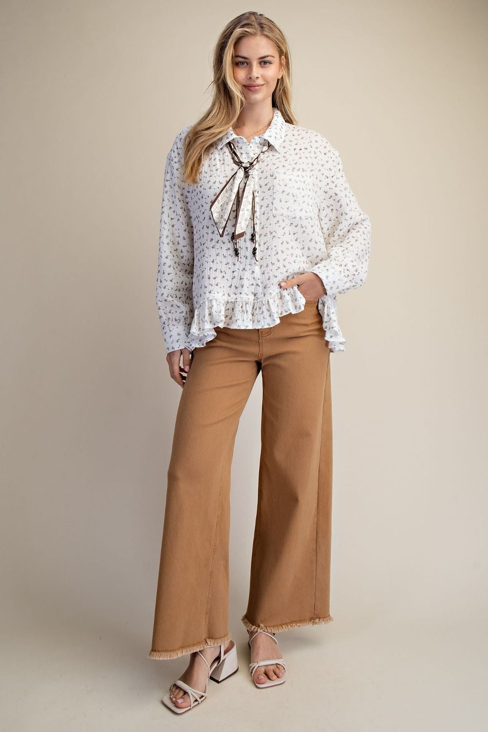 Woman wearing a patterned blouse with a bow and wide-leg pants on a beige background