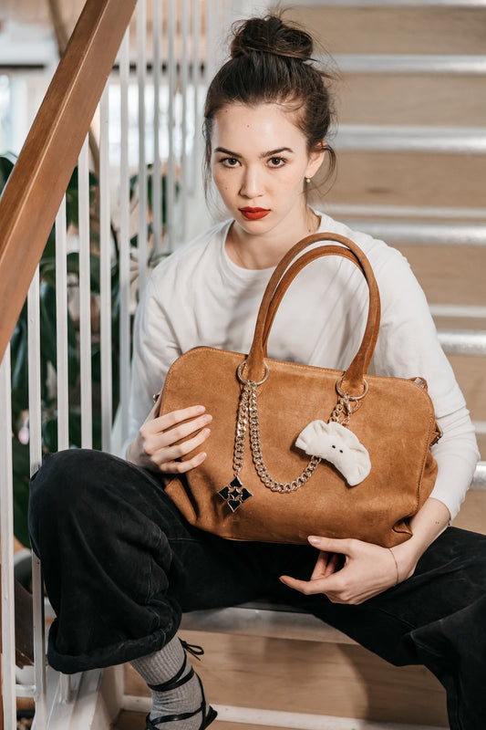 Woman holding a brown handbag with a decorative chain and charm, sitting on a staircase.