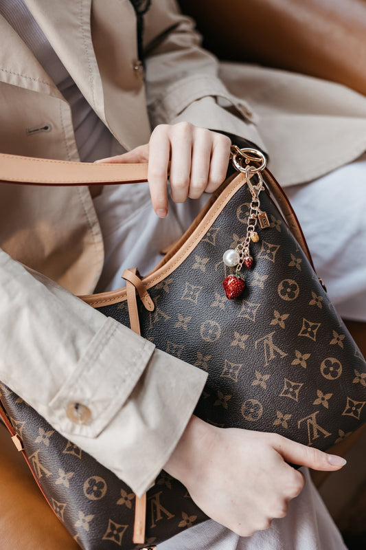 Person holding a handbag with a strawberry bag charm
