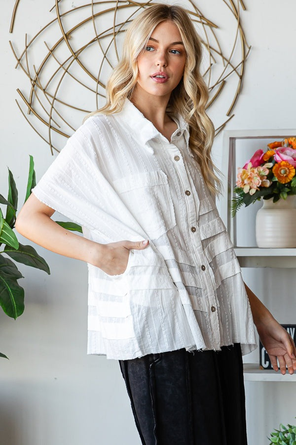 Woman wearing a layered outfit with a white top and striped vest in a home setting.