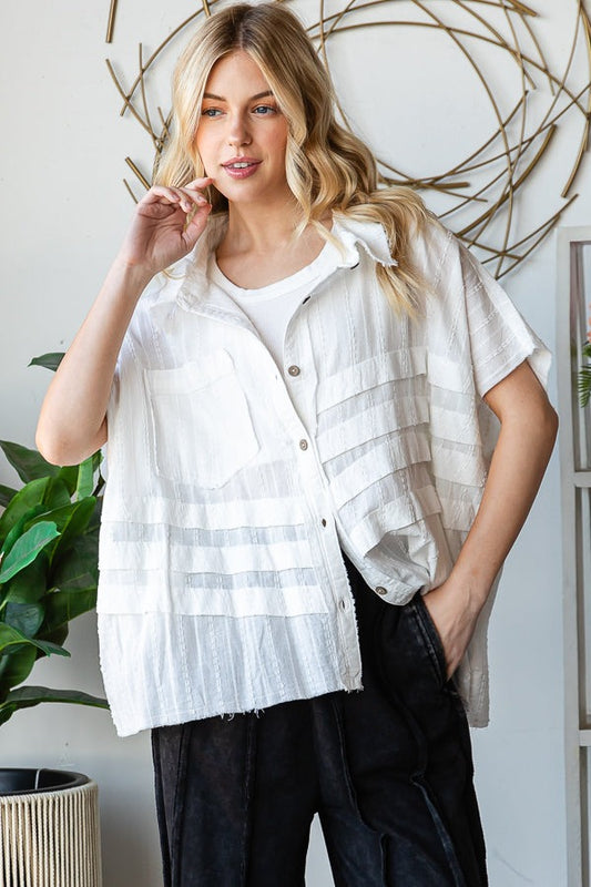 Woman wearing a white button-up shirt over a white top with black pants, standing indoors.
