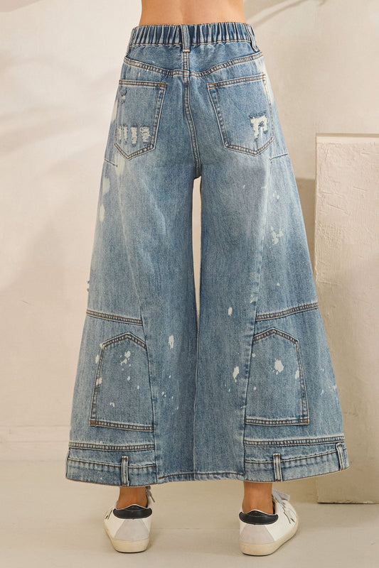 Wide-leg denim jeans with a light wash and distressed details on a neutral background.