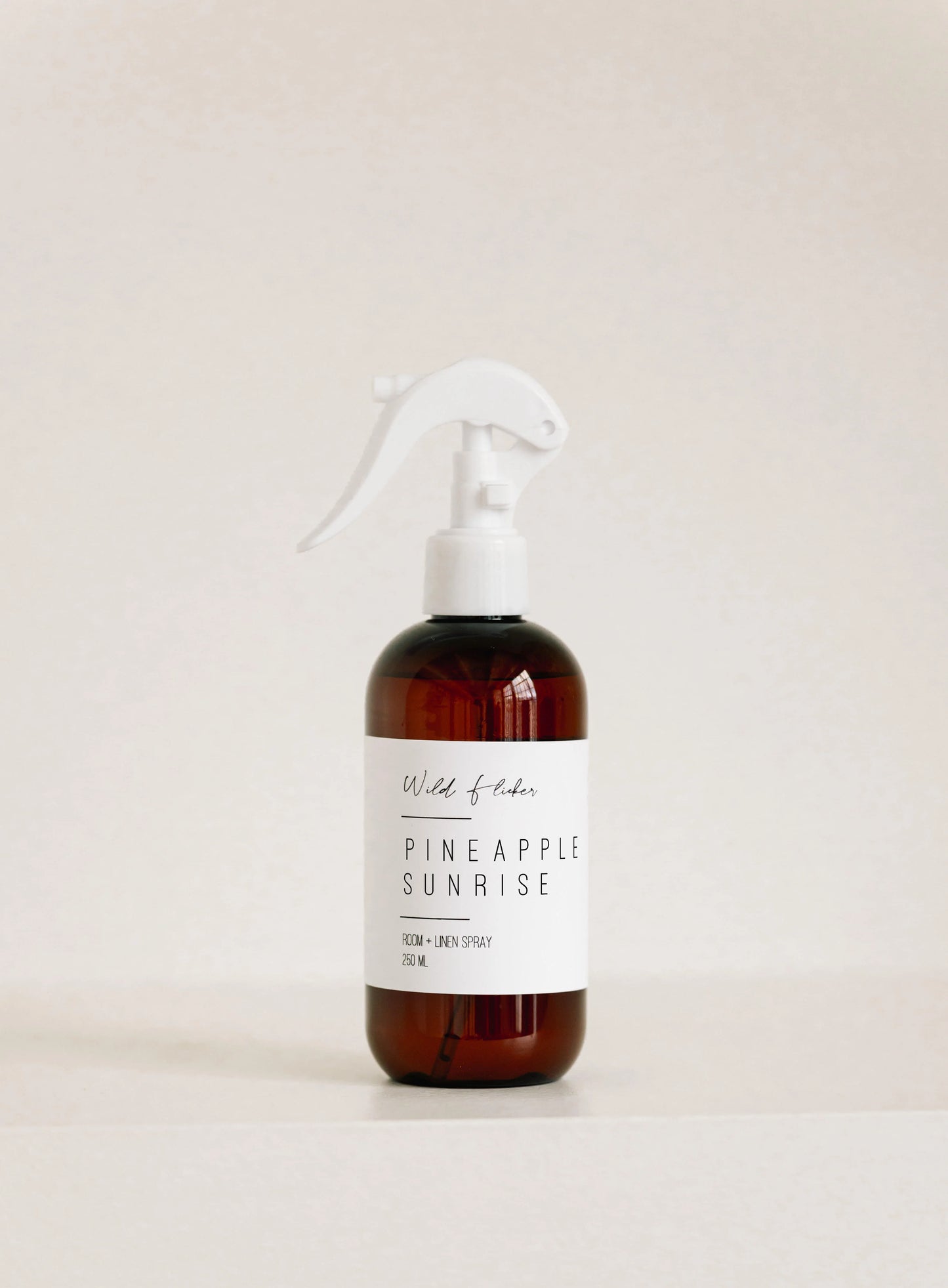 Brown room & linen spray bottle with a white label on a light beige background