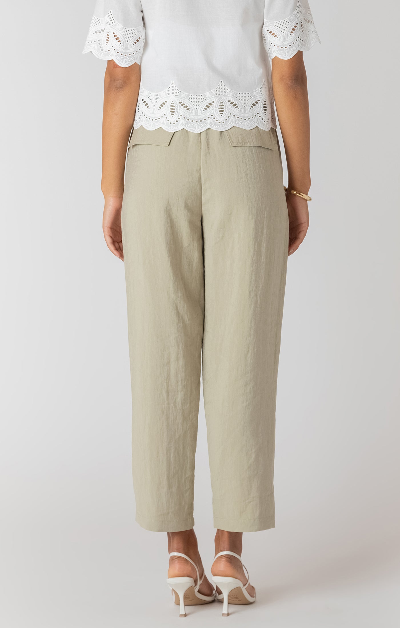 Person wearing beige pants and a white lace top on a plain background