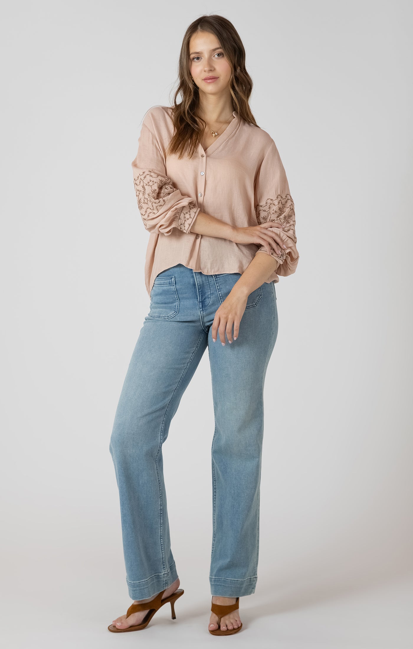 Woman wearing a beige lace top and blue jeans on a white background