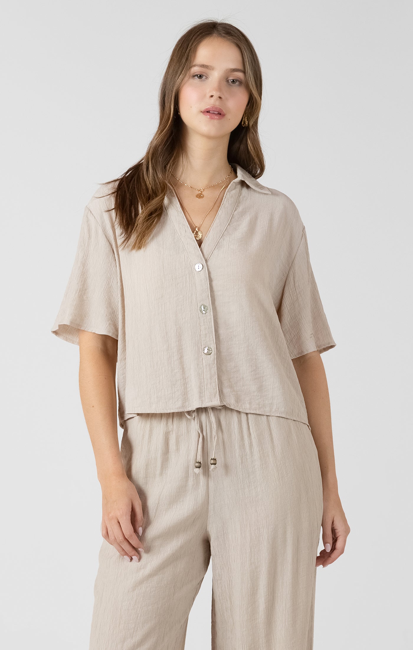 Woman wearing a beige short-sleeve shirt and pants on a white background