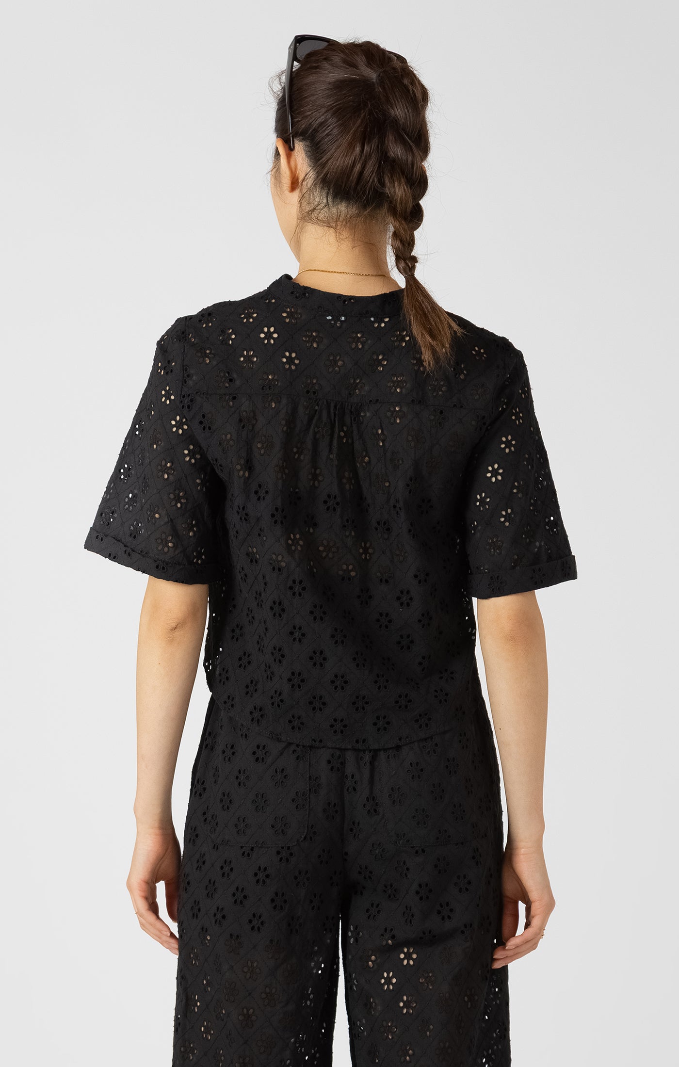 Person wearing a black eyelet blouse with a subtle pattern on a white background