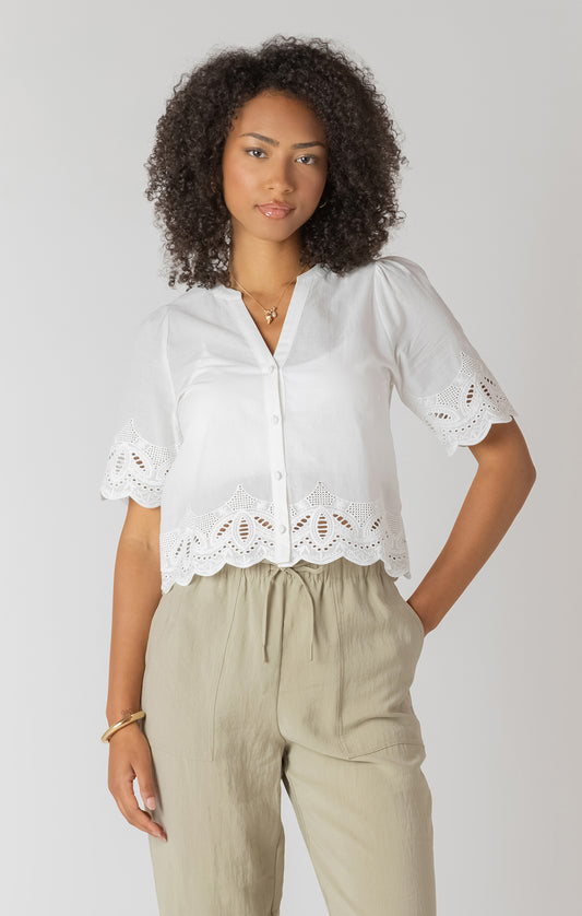Woman wearing a white blouse with lace details and beige pants on a plain background