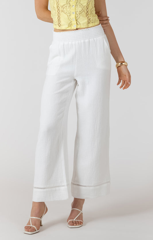 Person wearing white wide-leg pants and a yellow top on a plain background