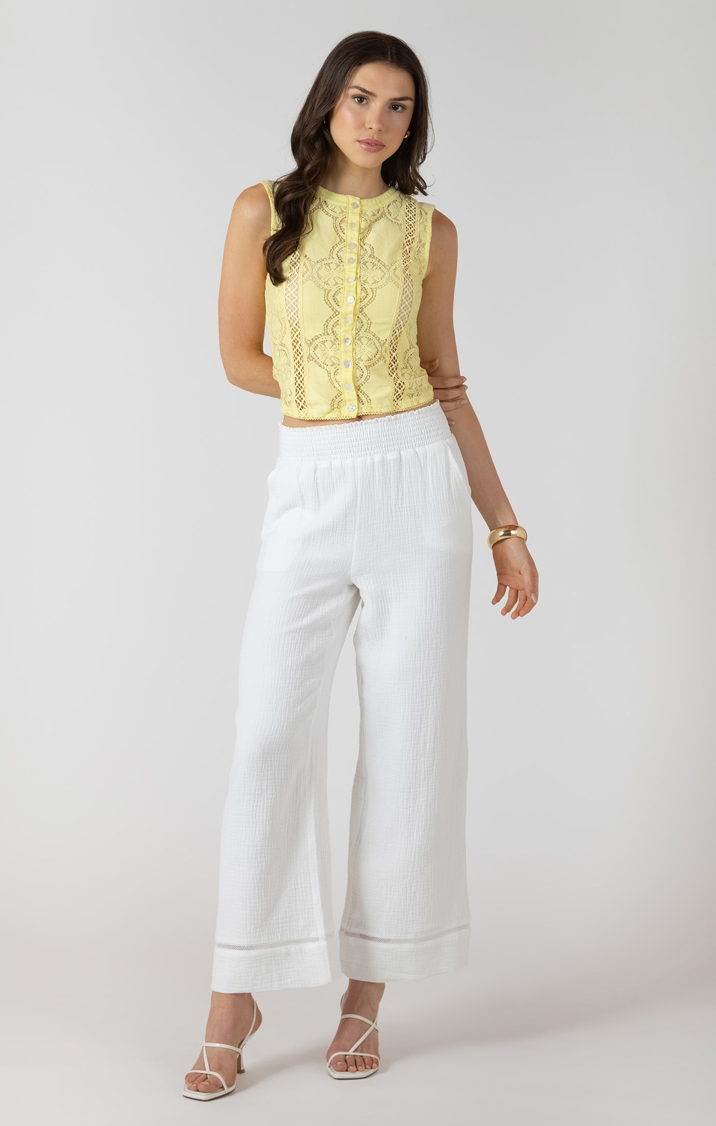 Woman wearing a yellow sleeveless top and white pants on a white background