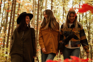 three women wearing fall shackets walking in the woods