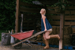 Women wearing a denim tunic and ruffle shorts while pushing a wheel barrow in a barn.