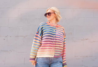 a women wearing a rainbow cardigan in front of a brick wall.