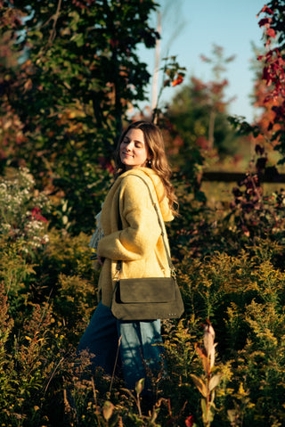 women standing in tall grass wearing a yellow cardigan, blue jeans and an olive bag