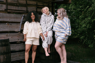 Three women wearing cozy matching lounge sets on a couch drinking coffee 