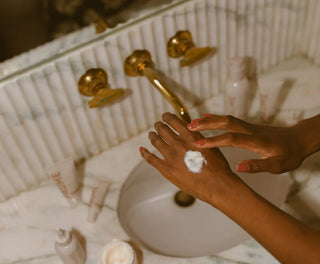 a women putting cream on her hands at the sink.