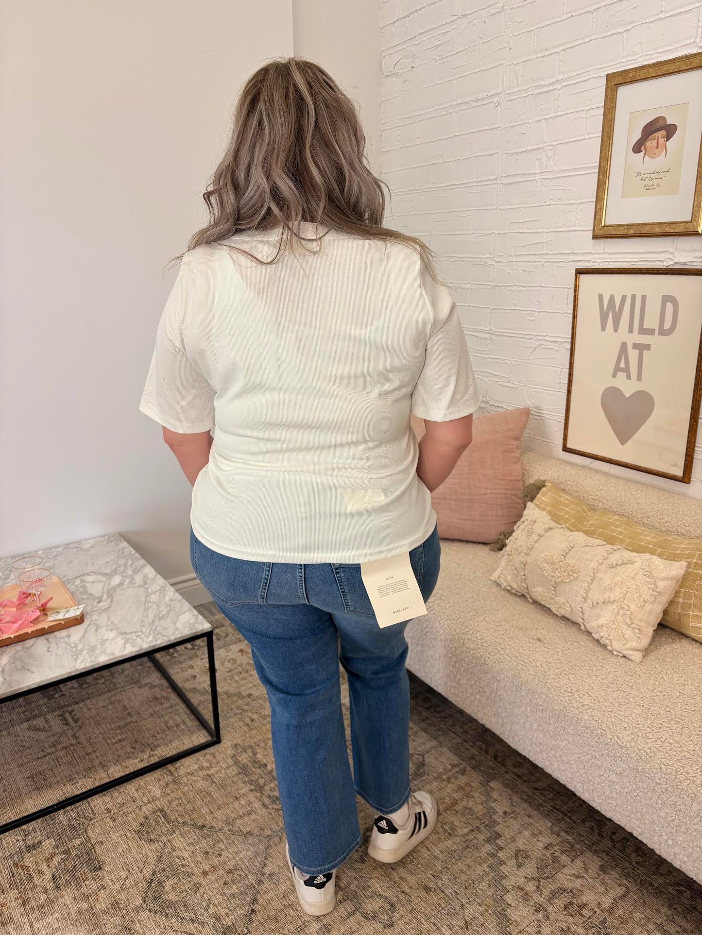 Person wearing a white shirt and blue jeans standing in a living room.