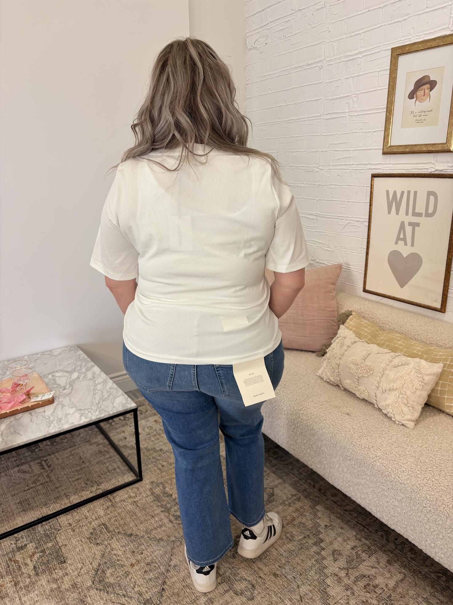 Person wearing a white shirt and blue jeans standing in a living room.